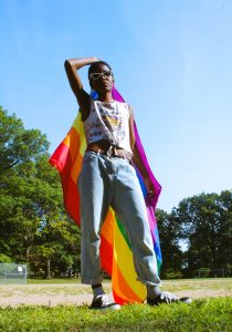 Image of person holding a rainbow pride flag behind them. This image depicts what an LGBTQ domestic violence survivor could look like. Working with a Black queer therapist in Baltimore, MD can help you overcome relationship trauma. | 21044 | 21204