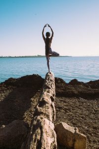 Image of a woman standing on a log and practicing a yoga pose. This image represents what someone may look like practicing mind-body medicine techniques learned from a holistic therapist in Baltimore, MD. 21204 | 21286 | 21044