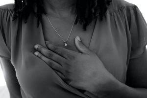 Black Woman holding her heart with her hand. This image represent what someone healing trauma may look like when they feel pain on their body and in their heart while practicing mind-body techniques learned during trauma therapy with a holistic therapist in Baltimore, MD. 21204 | 21286 | 21044