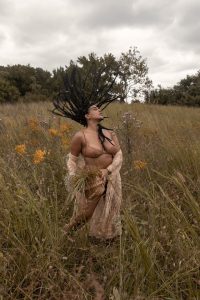 Image of a Black woman with dreadlocks moving in a flower field. This image represents what immersion may look like practicing mind-body medicine techniques learned from a holistic therapist in Baltimore, MD. 21204 | 21286 | 21044