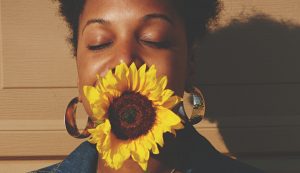 Image of a woman standing in the sunlight smiling with a sunflower. This image represents what someone may look like after meeting with a holistic therapist for EMDR therapy in Baltimore, MD. 21204 | 21286 | 21044