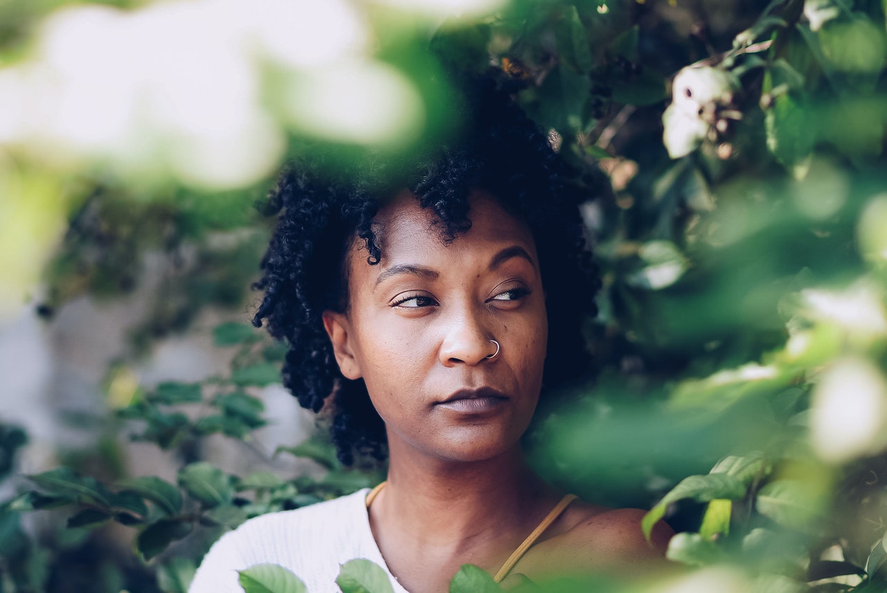 Image of a Black woman standing against a tree surrounded by green leaves. This image represents the hesitancy clients may feel before seeing an EMDR therapy. Meet with an EMDR therapist in Baltimore, MD today. | 21204 | 21286 | 21044