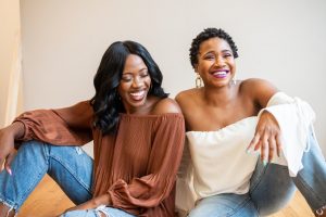  Image of two women sitting on the floor together smiling. This image illustrates the happiness you can find in with yourself and others after visits a trauma therapist in Baltimore, MD. Seeing a Black therapist can help you progress in therapy. | 21204 | 21286