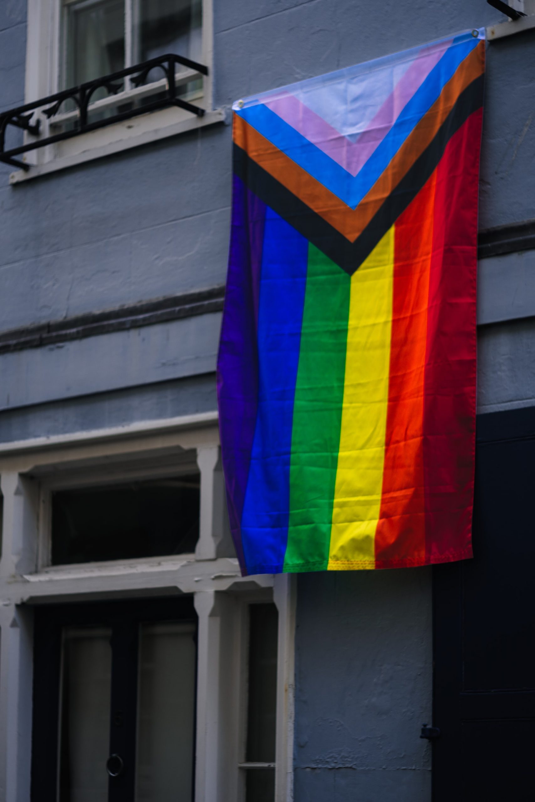 Image of a LGBTQIA+ flag handing from a pole outside of a building. This image represents the pride that LGBTQIA+ folks have when they express their authenticity after meeting with a Black, queer therapist. Meet with a trauma therapist in Baltimore, MD today. | 21204 | 21286 | 21044