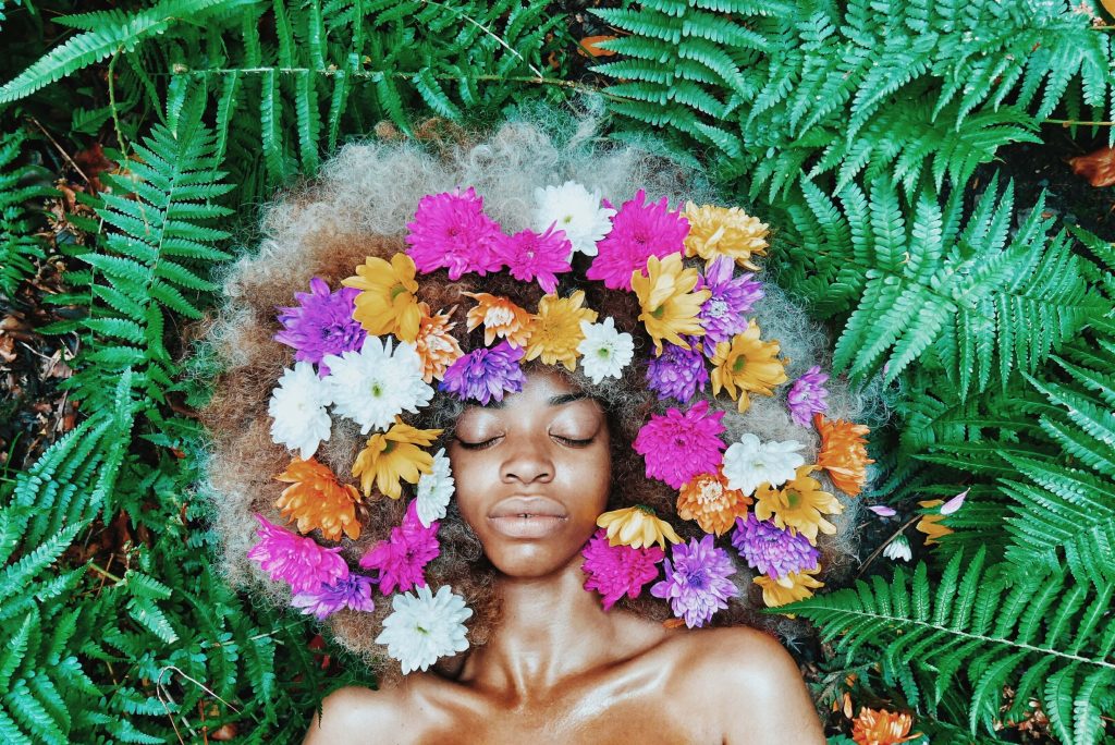 A beautiful black woman lies on a bed of ferns with flowers in her hair representing the peace that can be found with EMDR Therapy in Baltimore, MD.